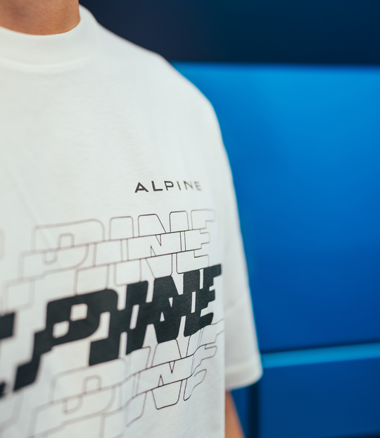 Close up of a white Alpine T shirt showing the chest graphic and logo against a blue background.