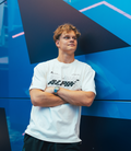 Man wearing white Alpine Formula One Team Silverstone oversized T shirt against a bright blue backdrop.