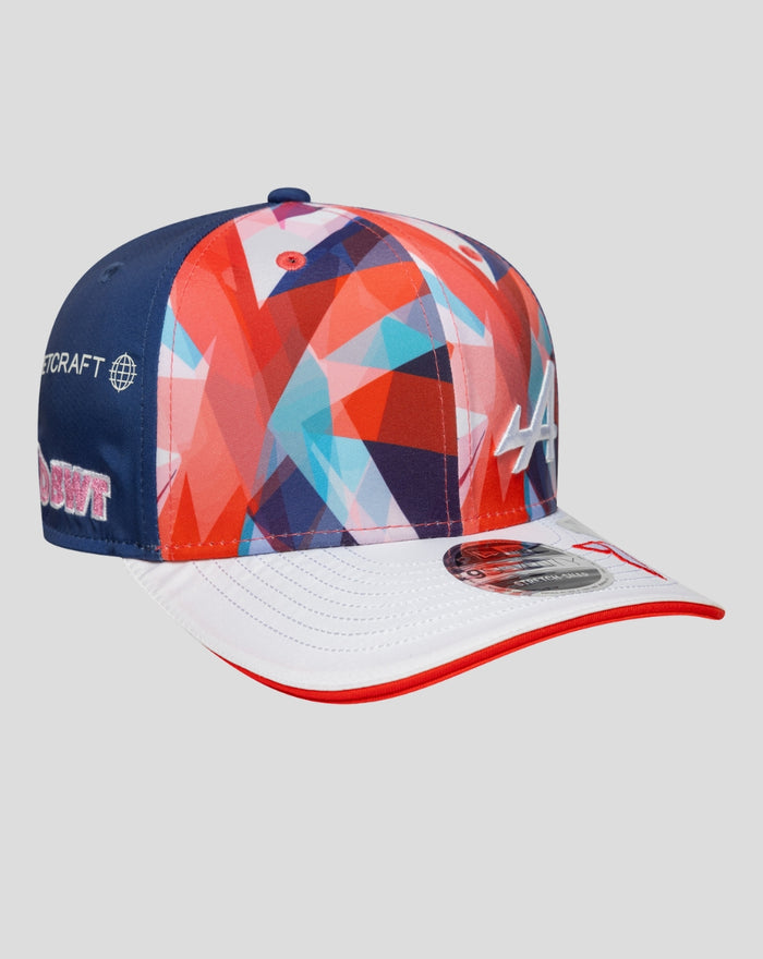 Angled side view of the cap showing the blue back panel, colorful crown, and white brim with red edge and sponsor logos along the side.