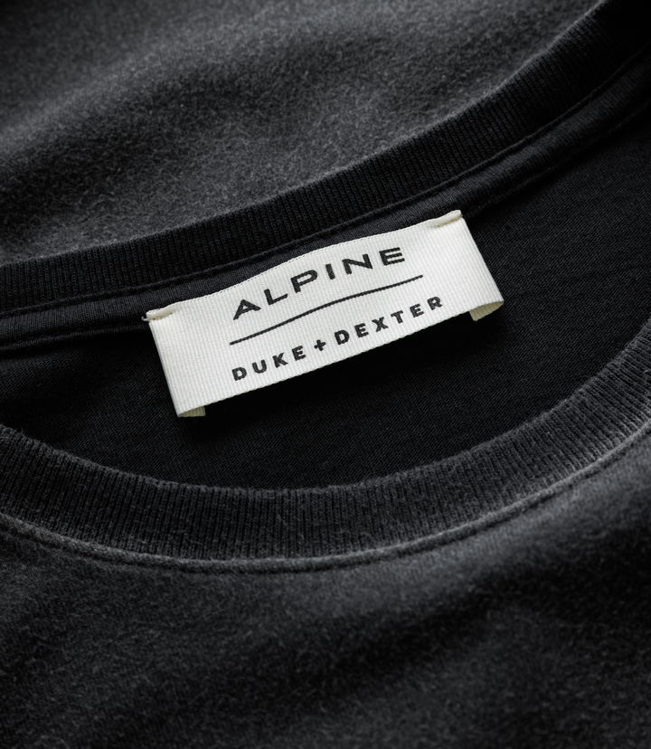 Close-up of white woven label on a black Duke and Dexter Helmet Washed Black T-shirt with Alpine branding.