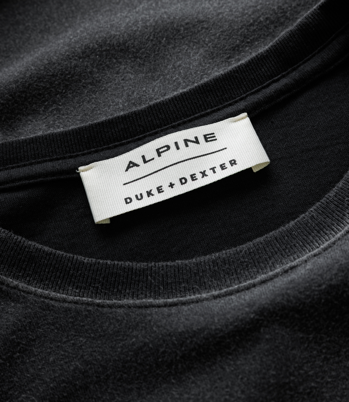 Close-up of white woven label on a black Duke and Dexter Helmet Washed Black T-shirt with Alpine branding.