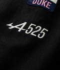 Close-up of a navy patch with pink Duke embroidery sewn onto a black jacket fabric