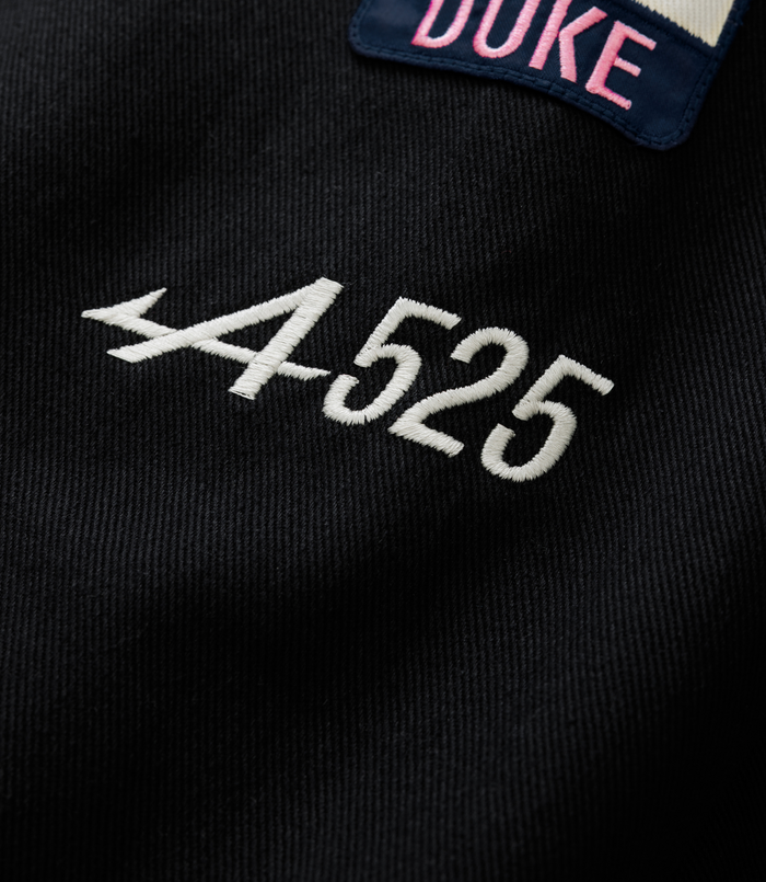 Close-up of a navy patch with pink Duke embroidery sewn onto a black jacket fabric