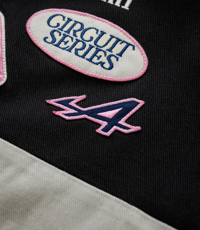 White oval patch with pink border and blue Circuit Series embroidery on black fabric