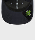 Close up of navy cap brim with pink edge and a green New Era circular patch sticker