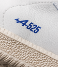 Close up of white leather sneakers with blue logo pattern on the strap and beige textured sole.