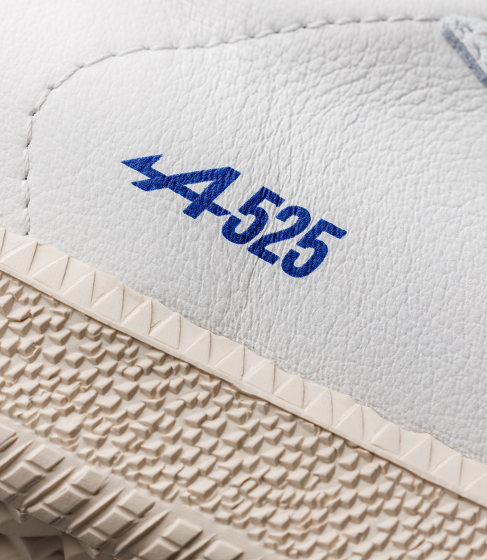 Close up of white leather sneakers with blue logo pattern on the strap and beige textured sole.