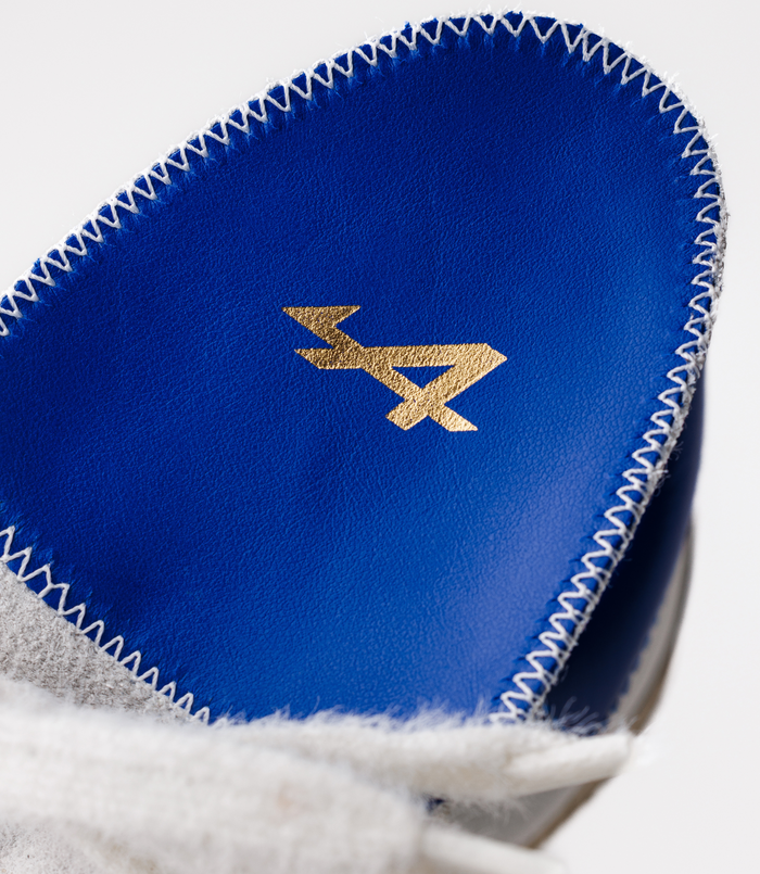 Blue leather sneaker upper with white stitching along the edge and a gold logo visible.