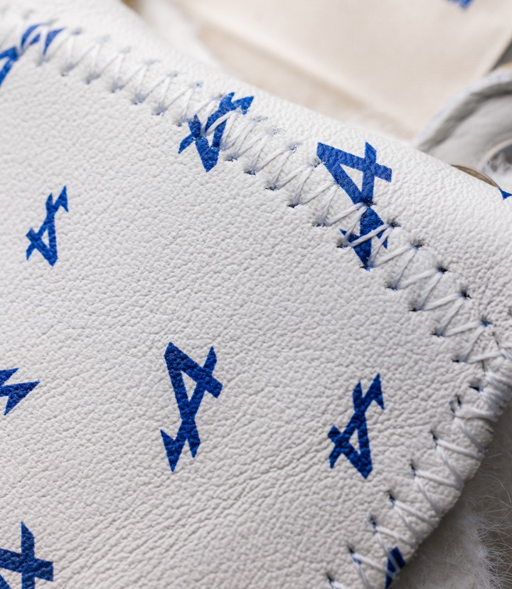 Close-up of white textured leather sneaker upper with blue embroidered geometric marks along the laces