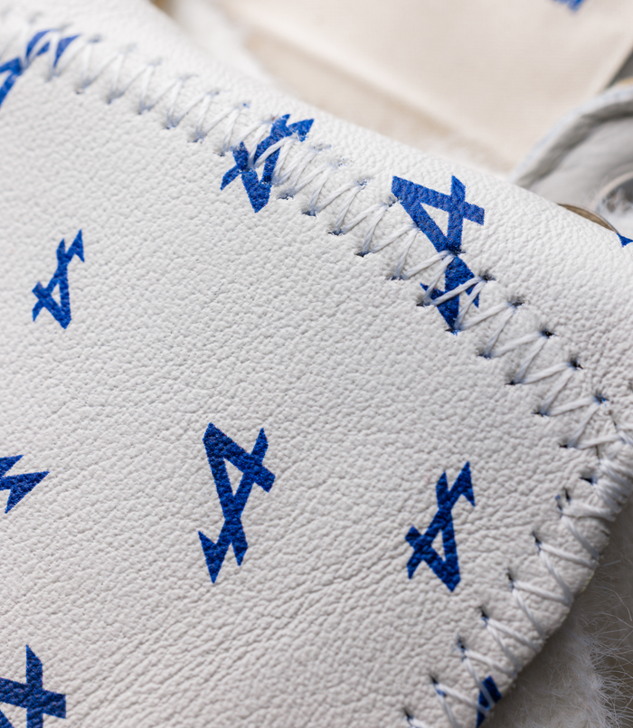 Close-up of white textured leather sneaker upper with blue embroidered geometric marks along the laces