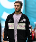 Male model wearing a Duke and Dexter racing jacket with pink Duke Racing script and various patches.