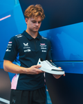 Young man in a BWT Alpine team polo holds a white Endstate sneaker against a blue backdrop.