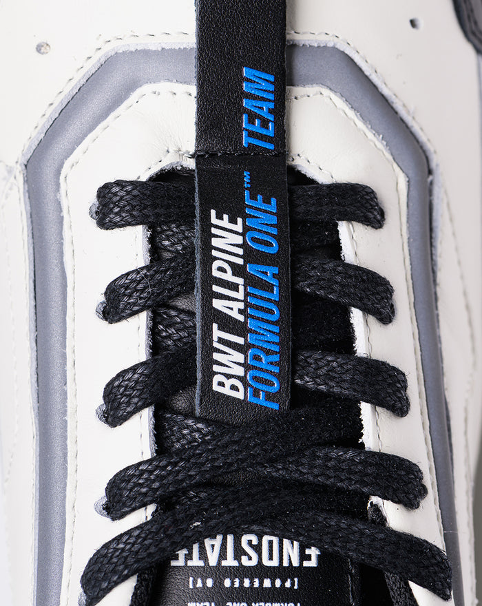 Close-up of a white Endstate sneaker showing black laces and a blue tongue tag with Alpine branding.