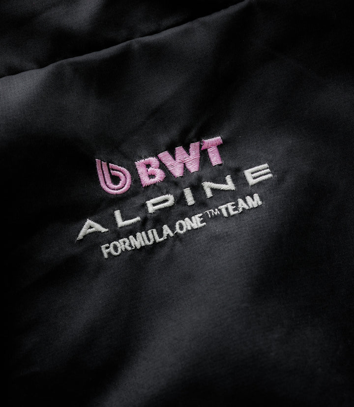 Close up of black fabric showing pink BWT Alpine logo and white Formula One Team embroidery.