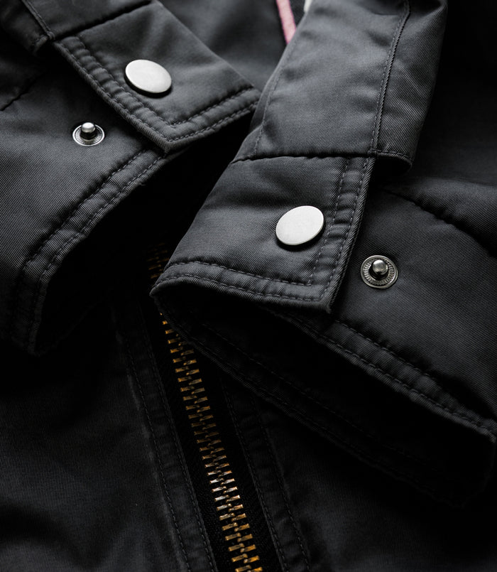 Close up of black trackside jacket fabric with metal snaps and visible zipper