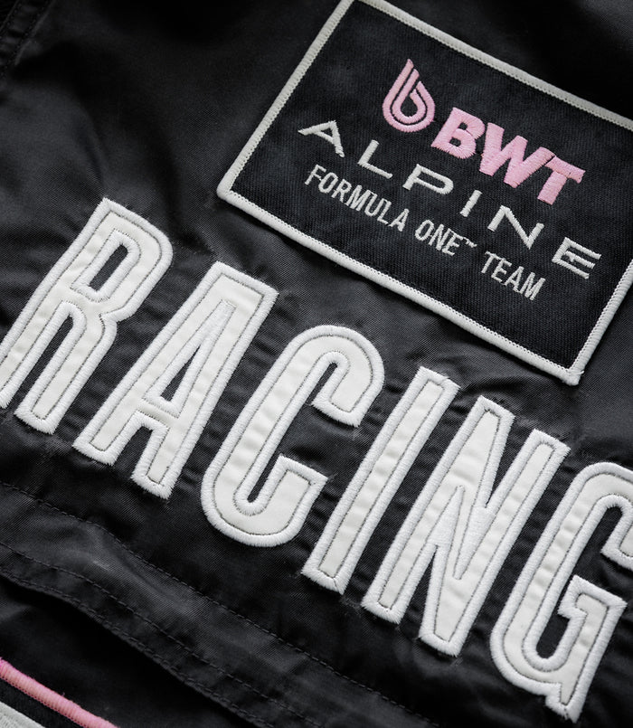 Close up of a black jacket showing the BWT Alpine patch with pink logo and Formula One Team embroidery.