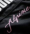Close-up of black trackside jacket showing white embroidered patch lettering and pink cursive script