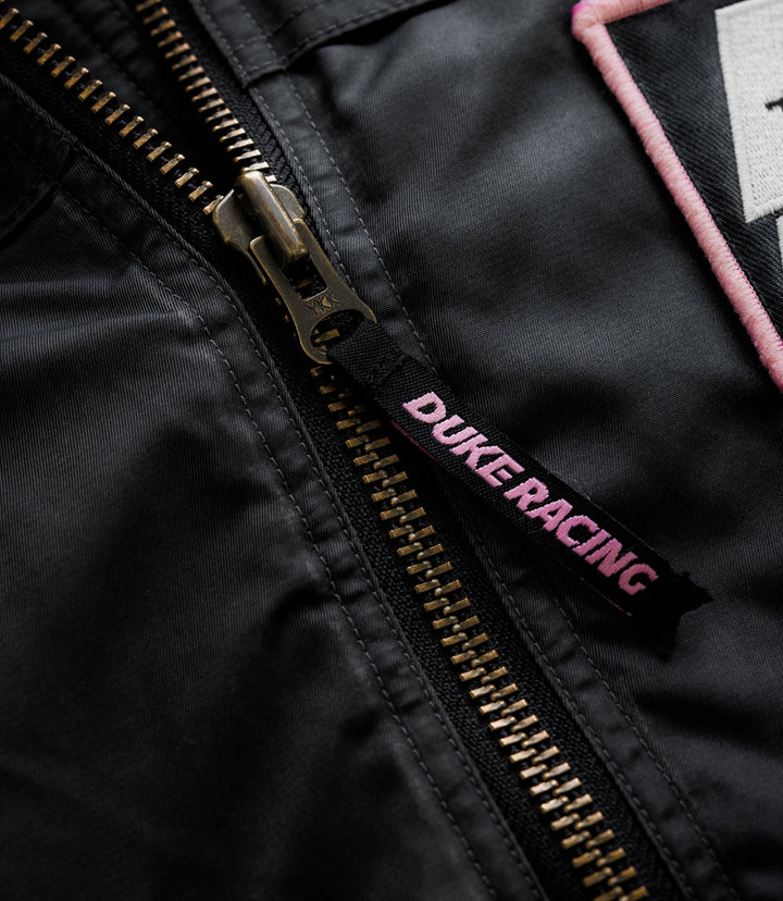 Close-up of brass zipper on black jacket with pink piping and woven label