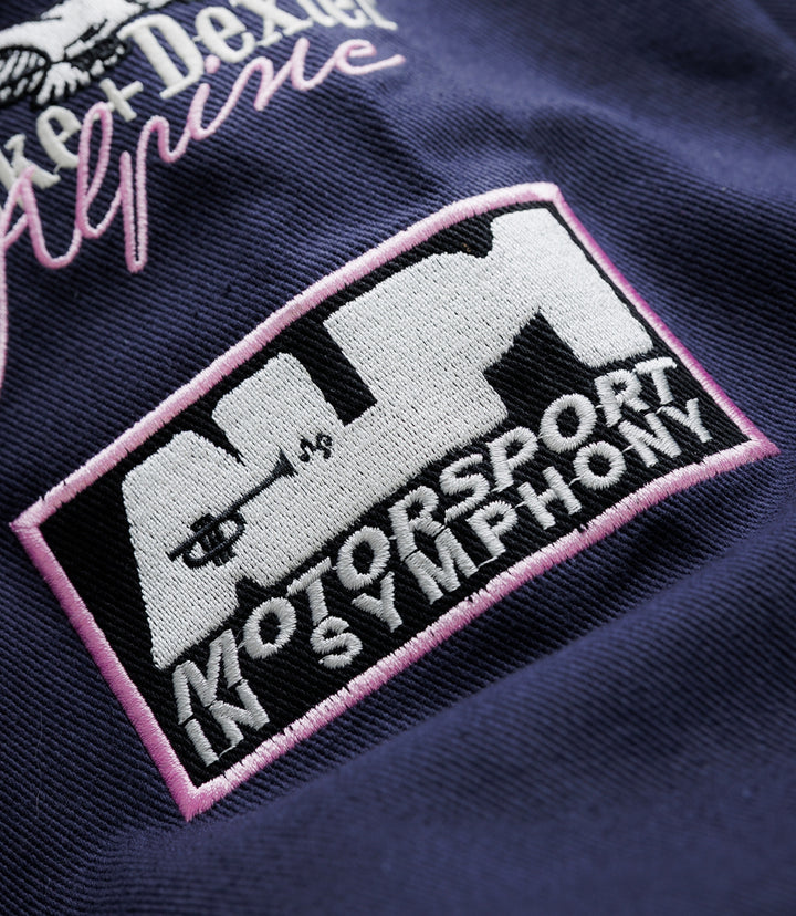 Close up of navy fabric featuring a stitched patch with pink border and a small pink-trim triangular badge.