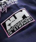 Close up of navy fabric featuring a stitched patch with pink border and a small pink-trim triangular badge.