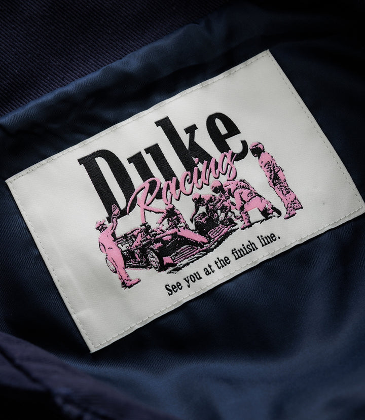 White stitched label on navy fabric with pink racing graphics and the Duke & Dexter branding
