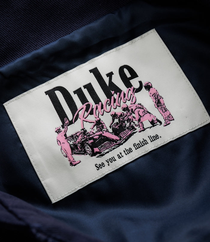 White stitched label on navy fabric with pink racing graphics and the Duke & Dexter branding