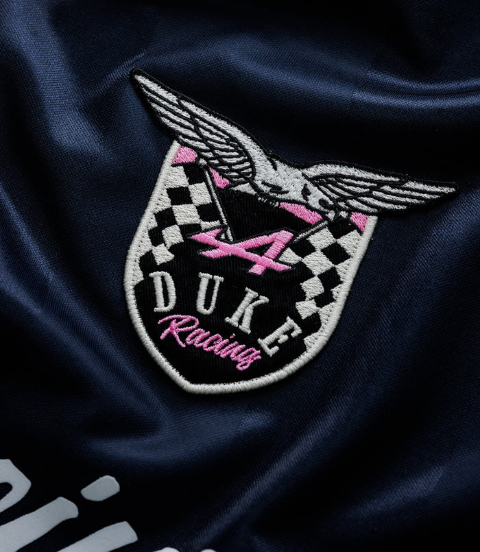 Close up of embroidered crest on navy fabric with wings and pink accents