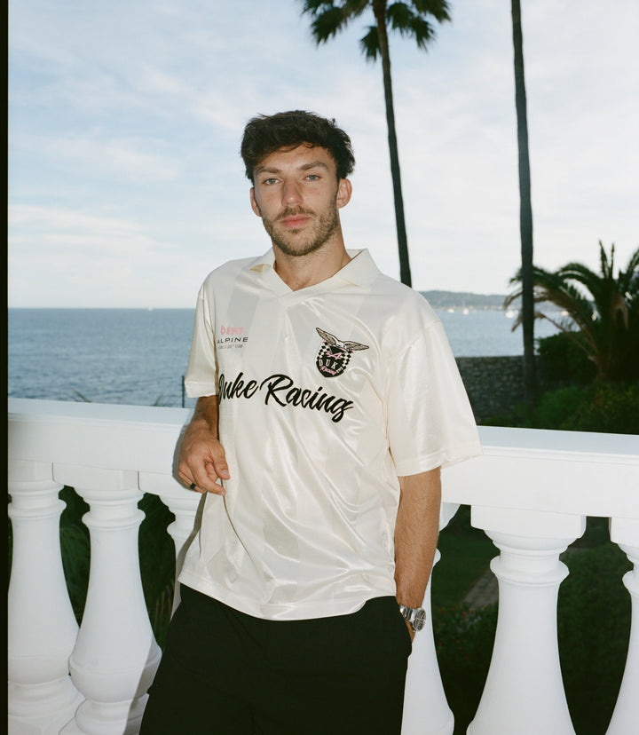 Man wearing a cream BWT Alpine Formula One Team Duke & Dexter jersey outdoors by the sea