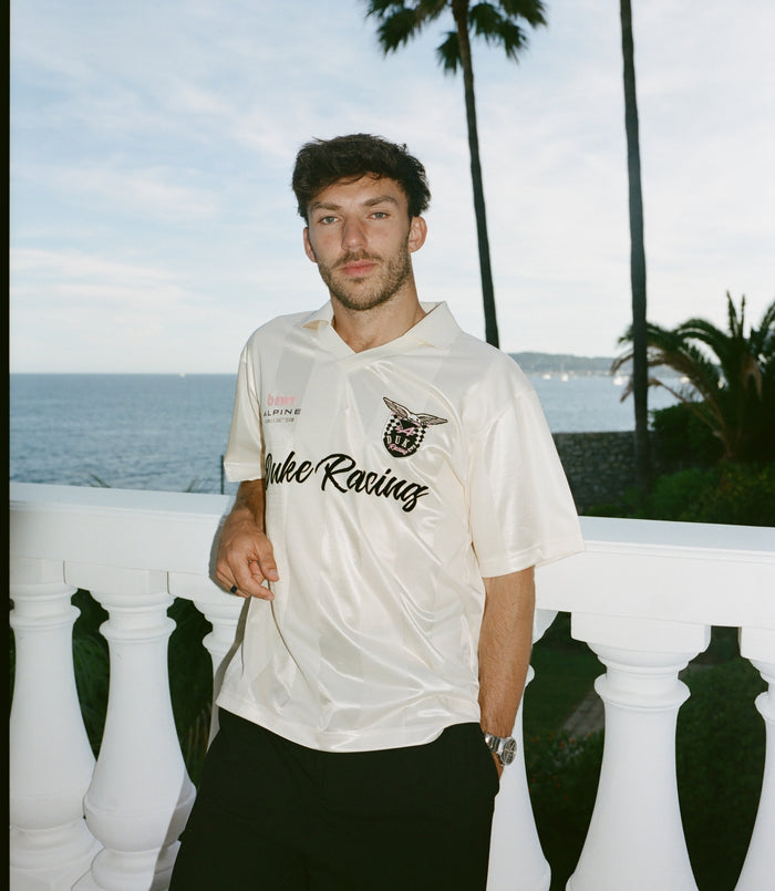 Man wearing a cream BWT Alpine Formula One Team Duke & Dexter jersey outdoors by the sea