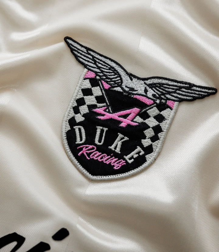 Close-up of a winged crest embroidery on cream satin fabric with pink accents
