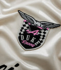 Close-up of a winged crest embroidery on cream satin fabric with pink accents