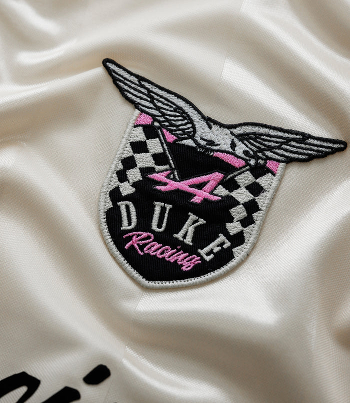 Close-up of a winged crest embroidery on cream satin fabric with pink accents