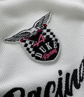 Close-up embroidered wing crest patch on white waffle fabric with checkered pattern and pink accents.