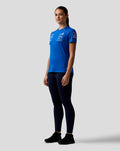 Woman in blue Official Women’s Formula One Team Set Up T Shirt with pink shoulder piping and front sponsor logos.