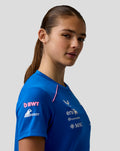 Profile view of a woman wearing blue Official Women’s Formula One Team Set Up T Shirt with pink shoulder piping and chest logos.