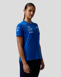Side view of a woman in blue Official Women’s Formula One Team Set Up T Shirt with logo graphics and pink shoulder piping.