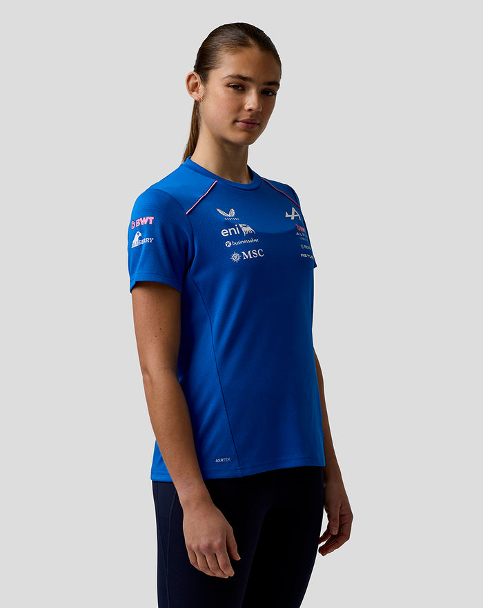 Side view of a woman in blue Official Women’s Formula One Team Set Up T Shirt with logo graphics and pink shoulder piping.