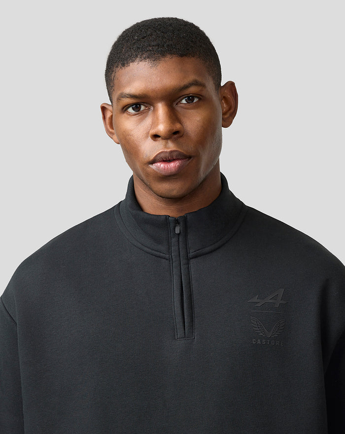Close-up of man in black BWT Alpine Castore funnel-neck quarter-zip top with chest logo.