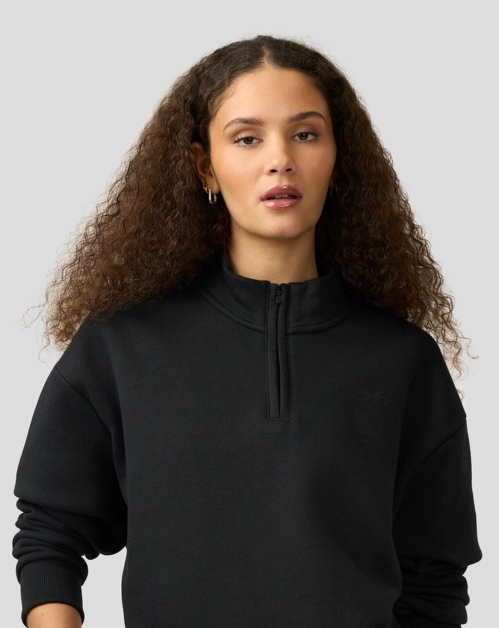 Woman wearing black Alpine Castore funnel-neck quarter-zip fleece with chest logo.