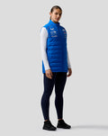 Three-quarter view of a female model in a blue BWT Alpine Formula One Team Gilet with pink shoulder piping and chest logos.