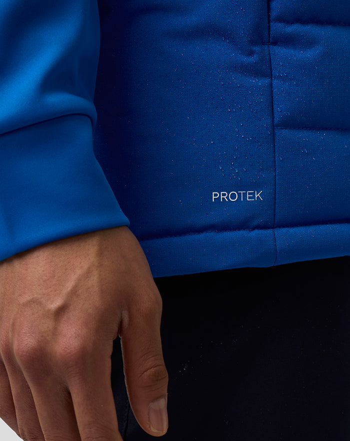 Close up of blue gilet fabric showing PROTEK label and a hand at the hem.