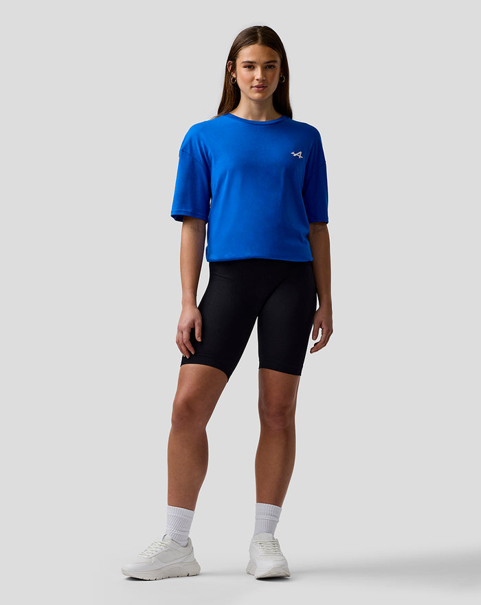 Front view of a woman wearing lapis blue BWT Alpine T shirt with embroidered A logo on the chest and black bike shorts