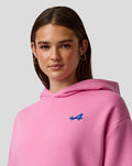 Portrait of a woman in a pink hooded sweatshirt with a blue embroidered A on the left chest.