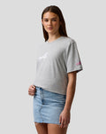 Woman wearing grey graphic T shirt with Alpine A chest print and pink A sleeve logo.