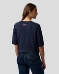 Back view of a woman wearing navy T shirt with pink Alpine branding at the upper back and a pink A logo on the left sleeve