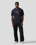 Front view of a man wearing navy T shirt with pink Alpine graphic on the chest and pink logo on the left sleeve