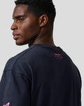 Back view of a man in a navy relaxed fit T shirt with pink Alpine logo on the upper back