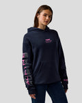 Female model wearing a navy BWT Alpine hoodie with pink embroidered A on the left sleeve and Alpine print on the right sleeve, chest logo and kangaroo pocket.