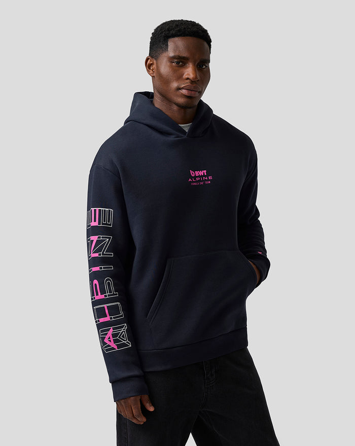 Male model wearing a navy Unisex Relaxed Fit Graphic Hoodie showing pink Alpine branding on chest, embroidered A on left sleeve, Alpine print on right sleeve, and a kangaroo pocket.